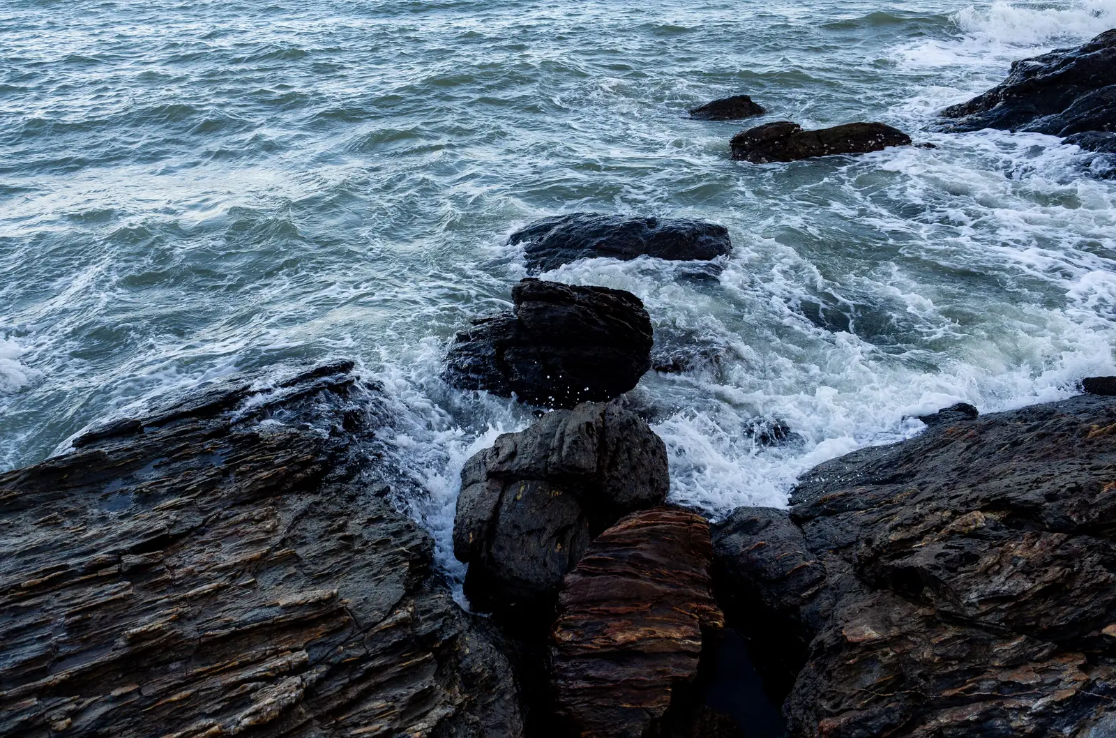 Waves breaking against dark rocks along a rugged shoreline